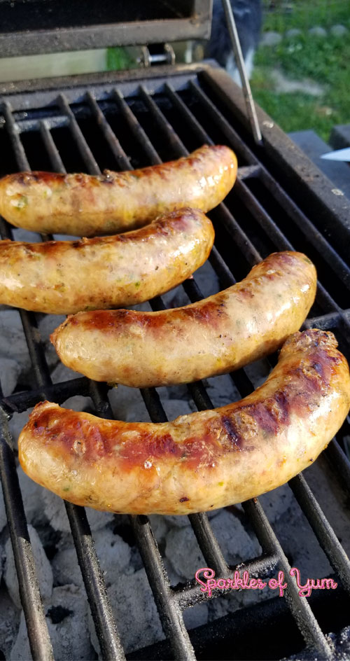 Four Homemade Jalapeno Cheddar Brats on a cast iron grate being grilled, over charcoal.