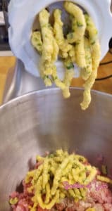 Jalapenos and cheese being ground together into a stainless steel bowl containing freshly ground pork.