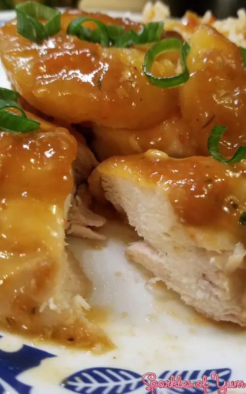 Close up view of cooked chicken cut open to show the interior texture. The chicken is covered in a light brown glaze and pineapple rings.