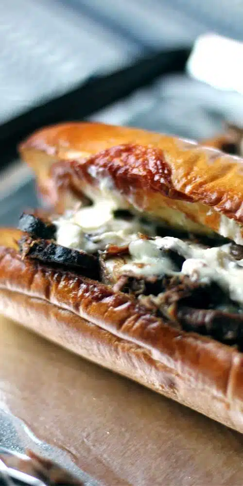 Slow wood smoked brisket on a cheesy garlic bread. You are going to fall in love with this sandwich.  Smoked brisket topped with melted cheese. The meat is in a baguette that has been split open. and has bits of toasted cheese on the edges.