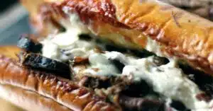 Smoked brisket topped with melted cheese. The meat is in a baguette that has been split open. and has bits of toasted cheese on the edges.