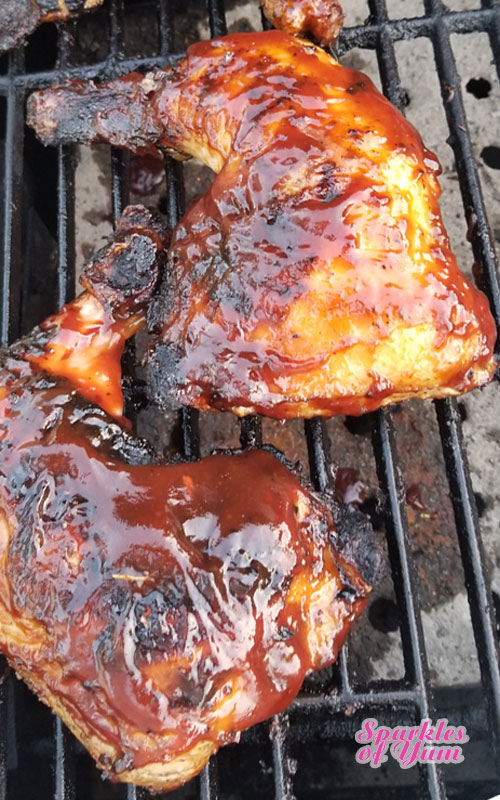 Two chicken leg quarters covered in barbecue sauce setting on cast iron grill grates.