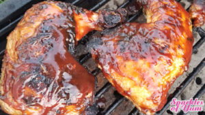 Two chicken leg quarters covered in barbecue sauce setting on cast iron grill grates.