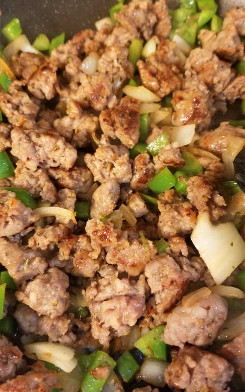 Sausage being browned with bell peppers and onion in a skillet.