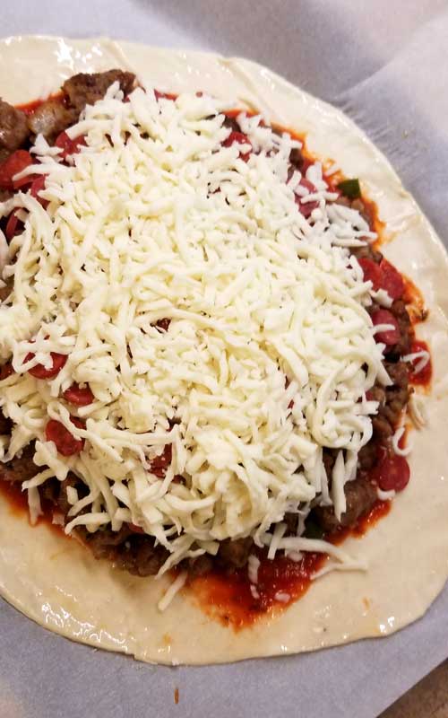 A pile of cheese on top of other filings. Everything is resting on the calzone's dough, before it is closed up.