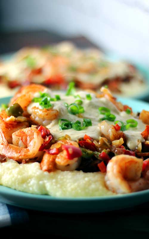 Shrimp and Grits on a blue plate. Red bell pepper, green onion, tasso ham, and cheese gravy  top the shrimp.