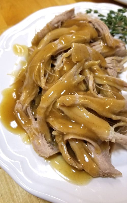 Overhead view of shredded Trisha Yearwood’s Crock Pot Pork Tenderloin covered in gravy, on a white plate.