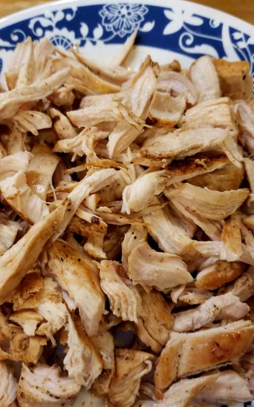 Close up view of shredded chicken on a white plate with a blue pattern on it.