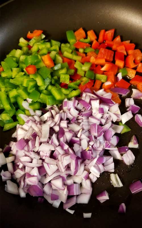 Diced green bell pepper, red bell pepper, and red onion resting in a black skillet.