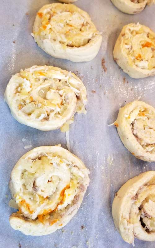 Uncooked Orange Pineapple Sweet Rolls on a sheet of wax paper. Coconut, orange, and pineapple can be seen in the rolls.