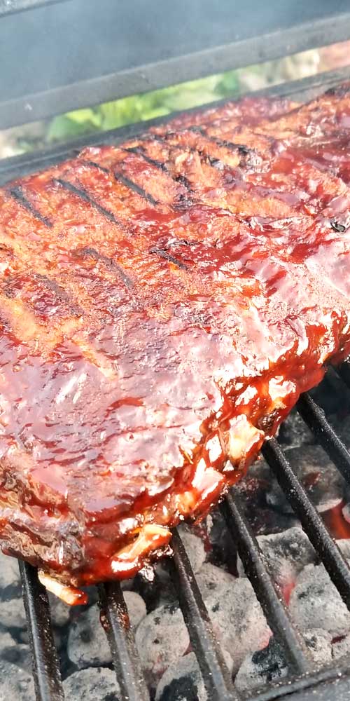 Close up of sauced BBQ ribs cooking on a charcoal grill