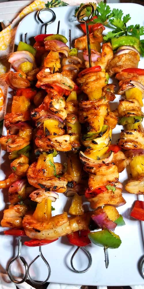 Grilled chicken, bell peppers, onion, and pineapple on metal skewers.