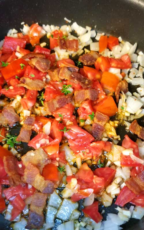 Tomato, bacon, onion, and garlic being cooked in a non-stick skillet.