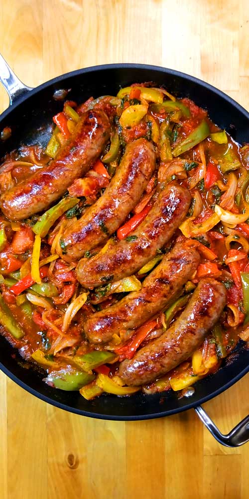 A skillet filled with five Italian sausages plus red, yellow, and green peppers.
