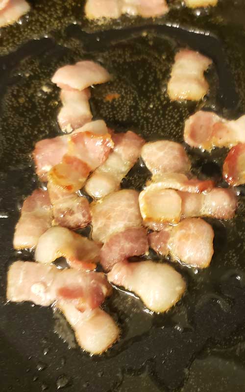 Small pieces of bacon frying in a skillet.