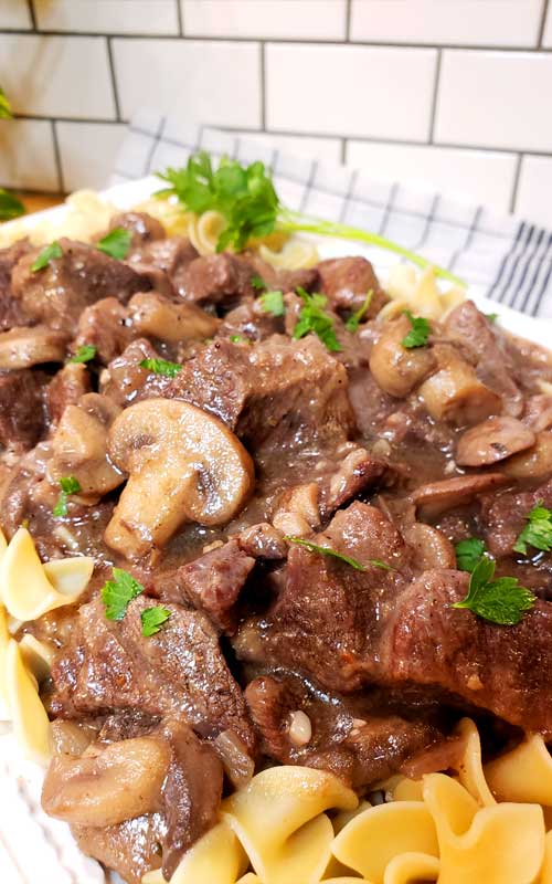 Diagonal view acrossed white platter holding Garlic Butter Beef Tips and Mushroom Gravy and egg noodles.