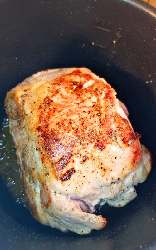 A browned pork roast sitting in a slow cooker.