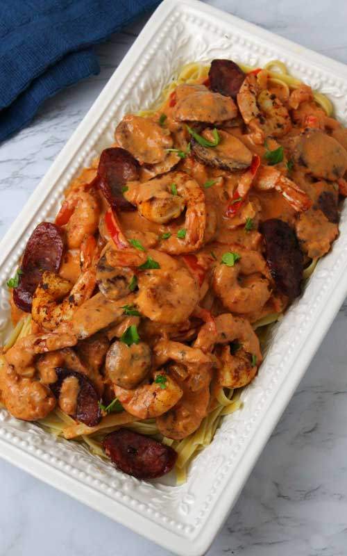 Top down view of a prepared Creamy Cajun Shrimp and Sausage Pasta in an oblong white serving platter.