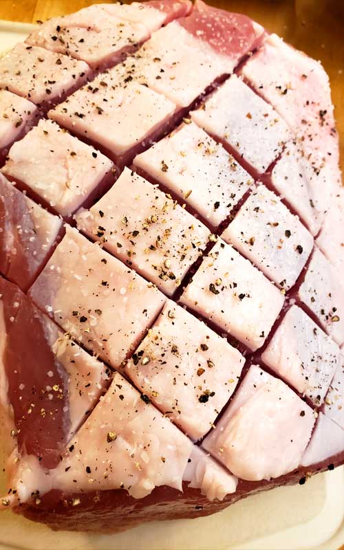 Close up image of scored and seasoned fat cap on uncooked pork roast.
