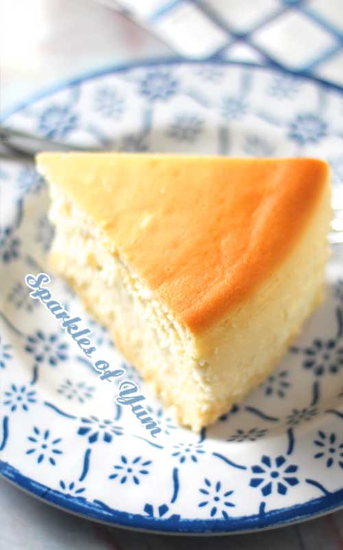 A top view of a slice of New York Cheesecake. The cheesecake is sitting on a white plate with a blue pattern.