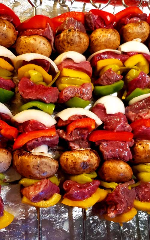 Steak, onion, bell pepper, mushrooms, and pepperoncini on metal skewers prior to being grilled.