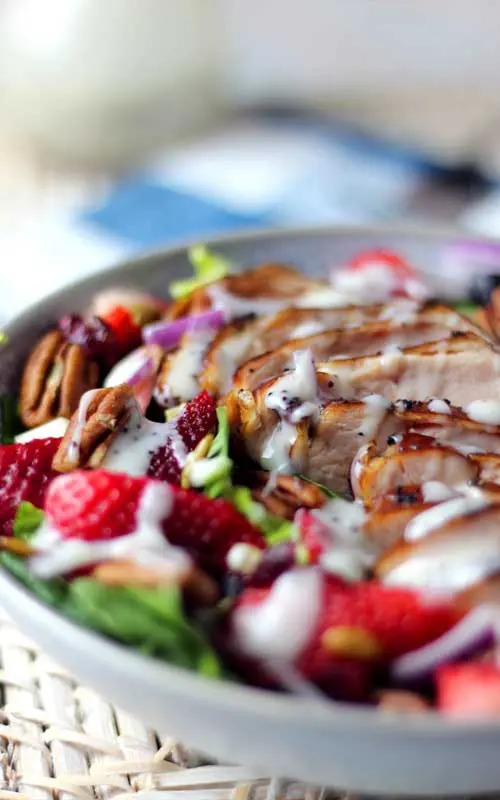 Close up view of a prepared Summer Strawberry Spinach Salad with Chicken in a white bowl. The image is composed to show the textures of all the ingredients.