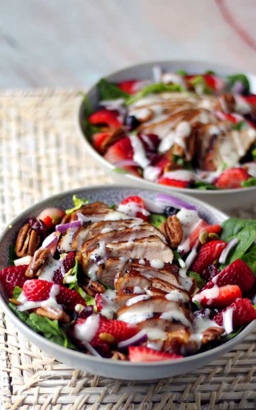 Two white bowls filled with prepared Summer Strawberry Spinach Salads.