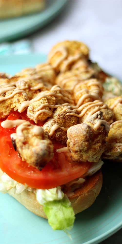 A close up view of a Shrimp Po'Boy with Rémoulade Sauce. The shrimp have been air fried, and are sitting atop the tomato on the sandwich.