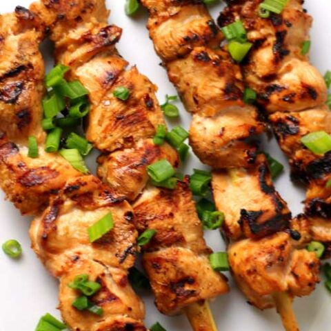 Four prepared Grilled Lemon Grass Chicken Skewers on a white platter.