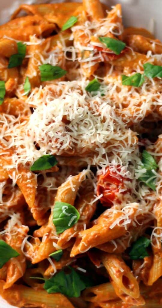 A top down view of penne pasta combined with a tomato sauce. The dish is covered with melting, grated cheese.