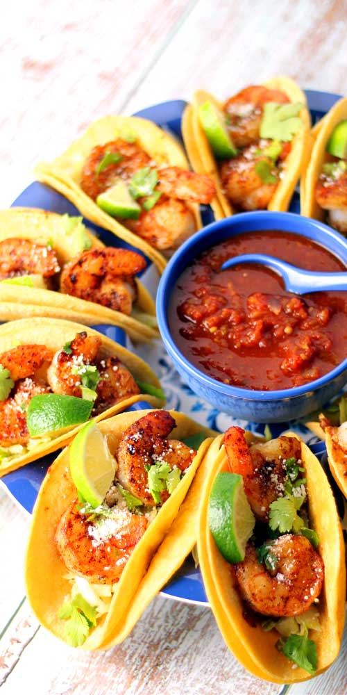 Shrimp tacos arranged around a blue bowl filled with salsa.