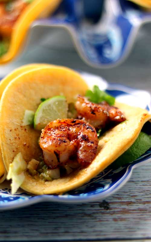 A shrimp street taco is sitting on a blue and white plate.