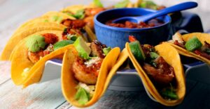 Shrimp tacos arranged on a plate. A blue bowl filled with salsa is in the center of the plate.