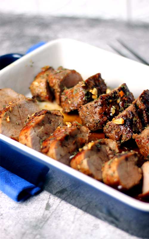 A cooked, sliced pork tenderloin resting in a blue and white baking dish.
