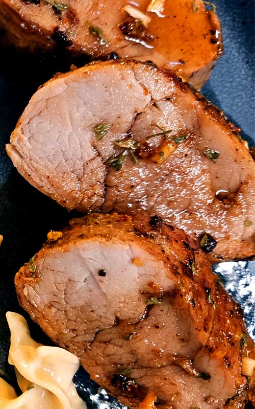 Three cooked pieces of pork tenderloin on a dark blue plate.