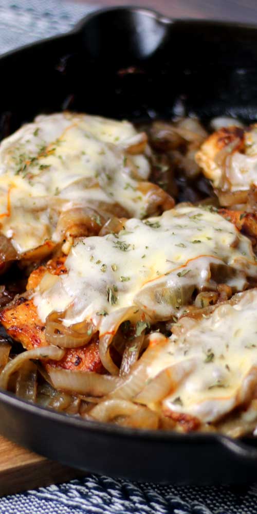 Four pieces of cooked chicken breast in a cast iron skillet. Each piece of chicken is covered in melted cheese.