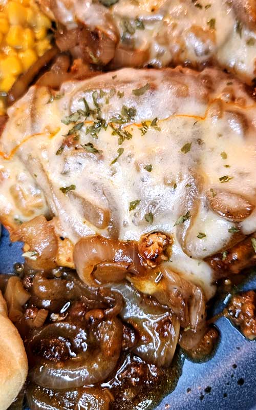 Melted cheese covering a cooked chicken breast. Caramelized onions and gravy can also be seen.