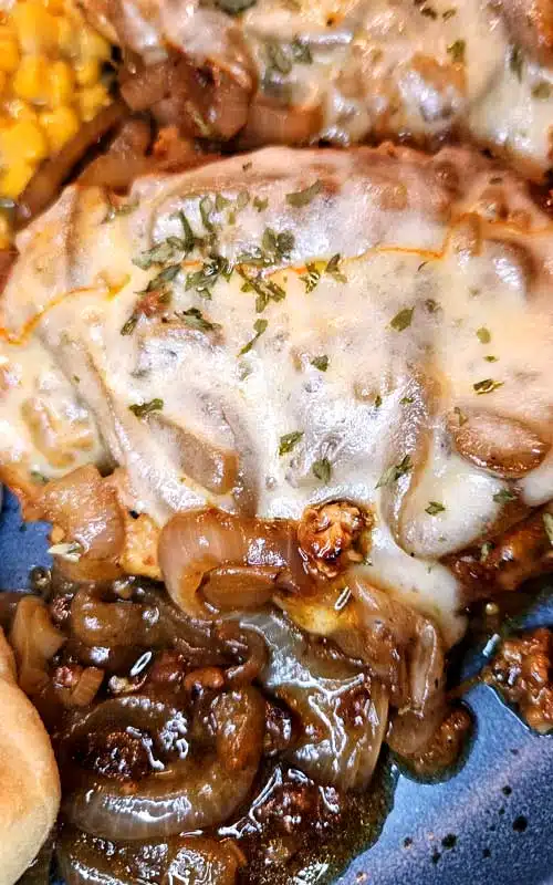 Melted cheese covering a cooked chicken breast. Caramelized onions and gravy can also be seen.