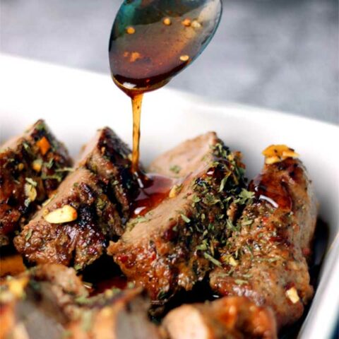 Hot honey being drizzled over a sliced pork tenderloin. The meat is in a white serving dish.