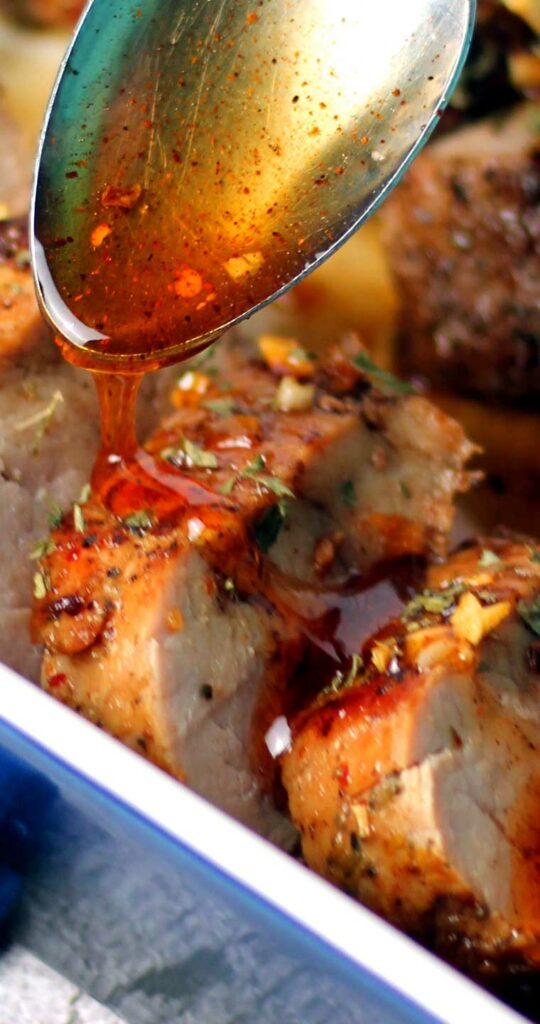 Close up image of a spoon drizzling hot honey over a sliced, cooked pork tenderloin.