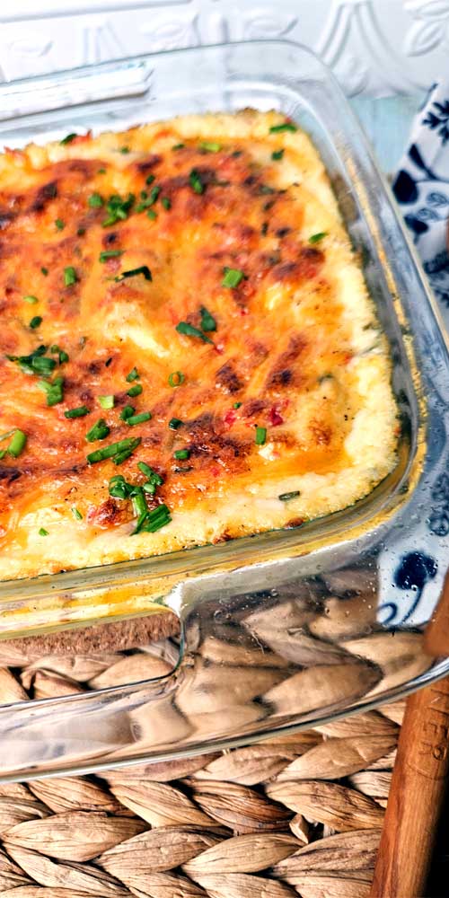 A clear baking dish filled with mashed potatoes that are topped with browned,melted cheese and chives.