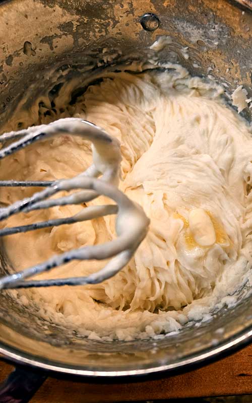 Whipped mashed potatoes in a metal mixing bowl. The mixer beaters are on the left edge of the image.