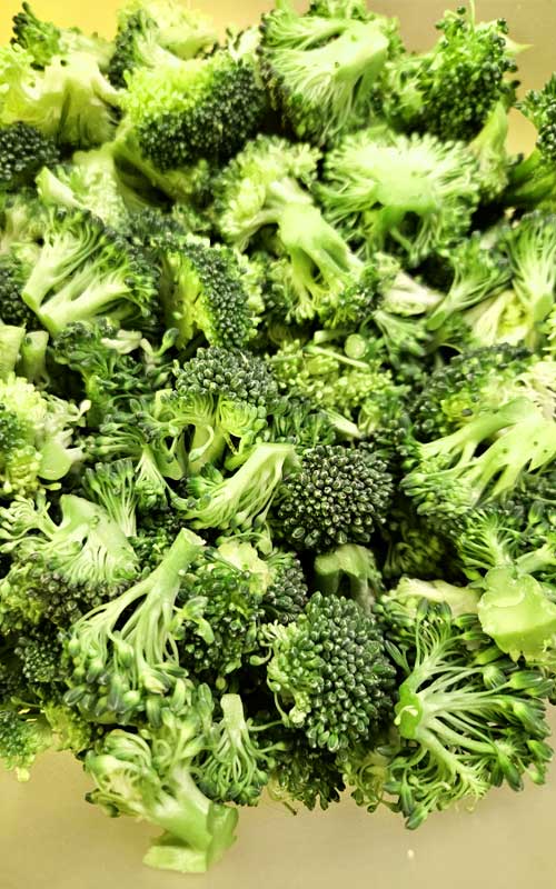 Overhead image of broccoli florets in a clear glass bowl.