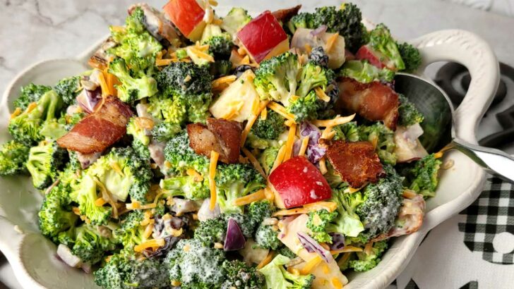 Broccoli, apples, cheddar cheese and bacon in a white bowl. The image is zoomed in to highlight the texture of the broccoli and dressing.
