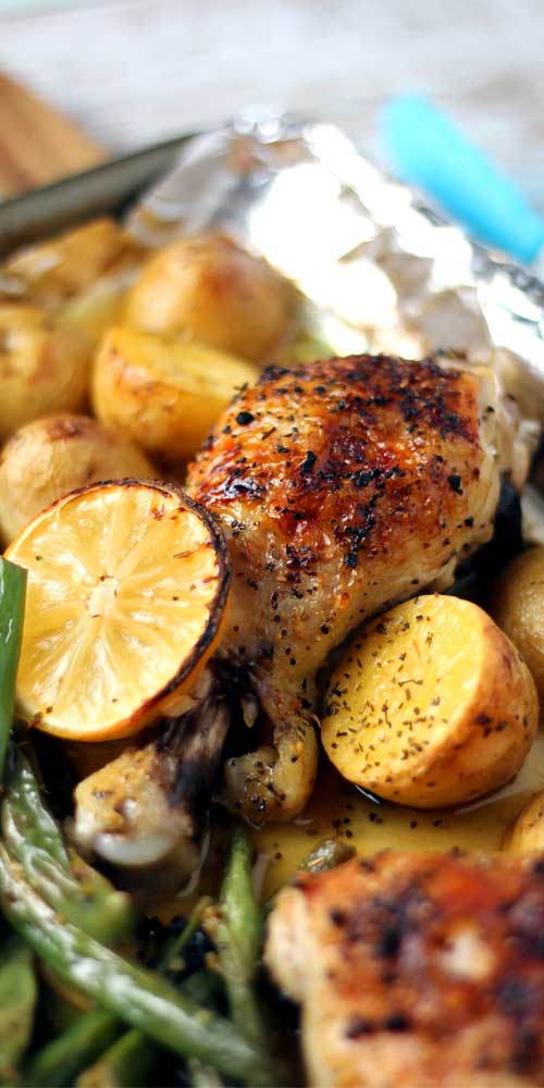 Cooked chicken, lemons, potatoes, and green beans on aluminum foil.