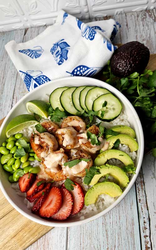 Overhead view of a white bowl filled with shrimp, avocado, strawberries, and cucumber.