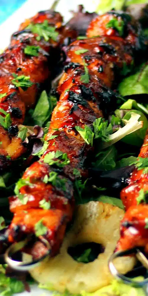 Grilled chicken and pineapple chunks on a metal skewer. The chicken and pineapple are covered in a reddish glaze.